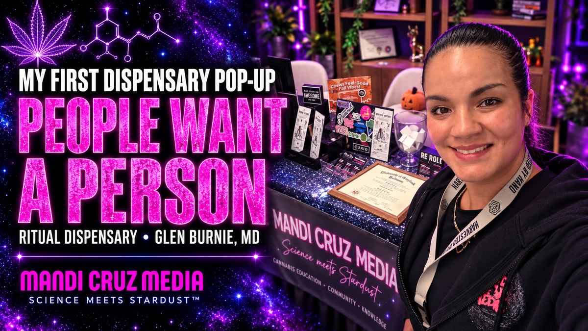 Mandi smiling beside her cannabis education table at Ritual Dispensary, with the Mandi Cruz Media banner and framed degree on display.