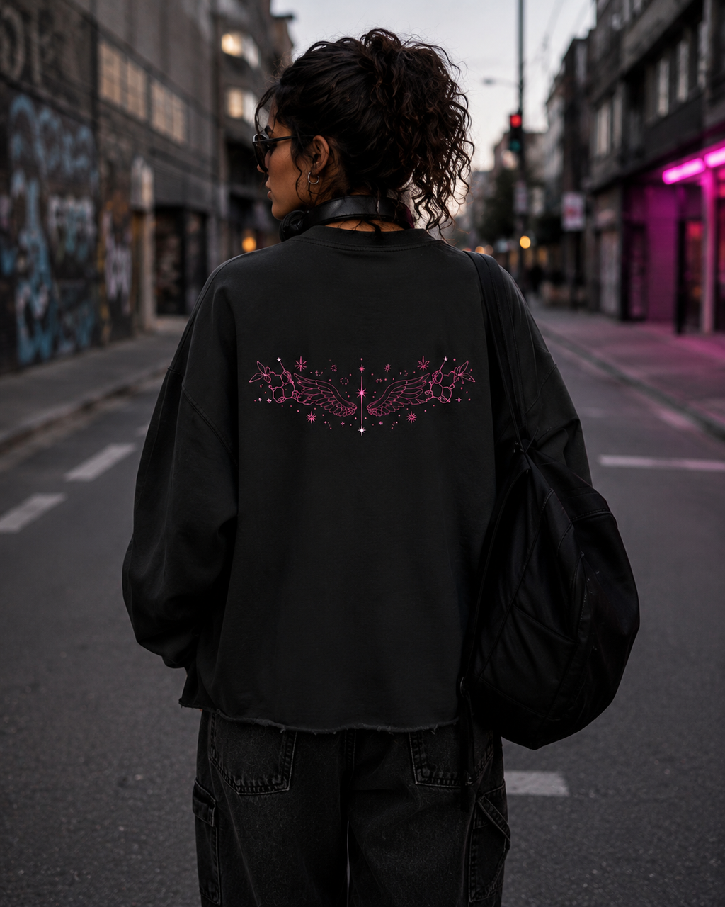 Back street-style view of the black Mandi Cruz Media boxy sweatshirt displaying the pink winged cosmic artwork.