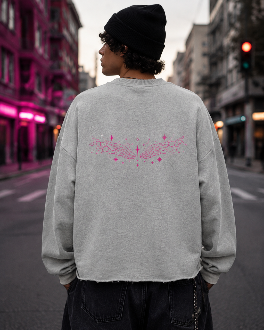 Man shown from behind wearing the Flower Gray oversized sweatshirt with pink winged celestial artwork on a neon-lit city street.