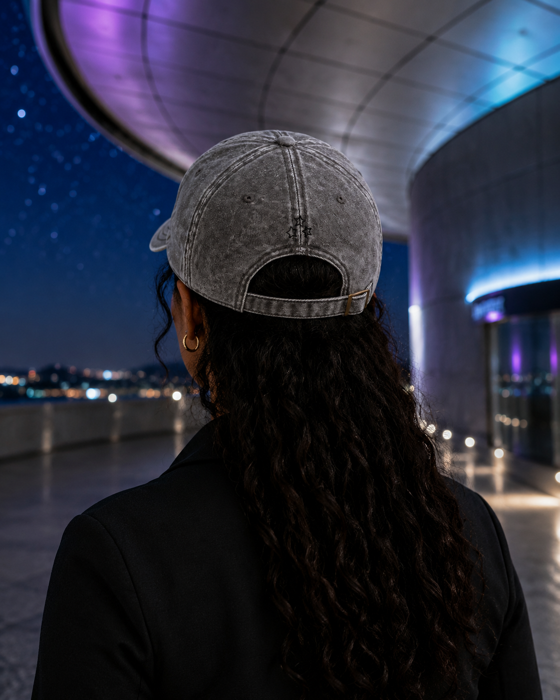 Rear view of a woman wearing the charcoal grey cap with three embroidered stars and an adjustable strap.