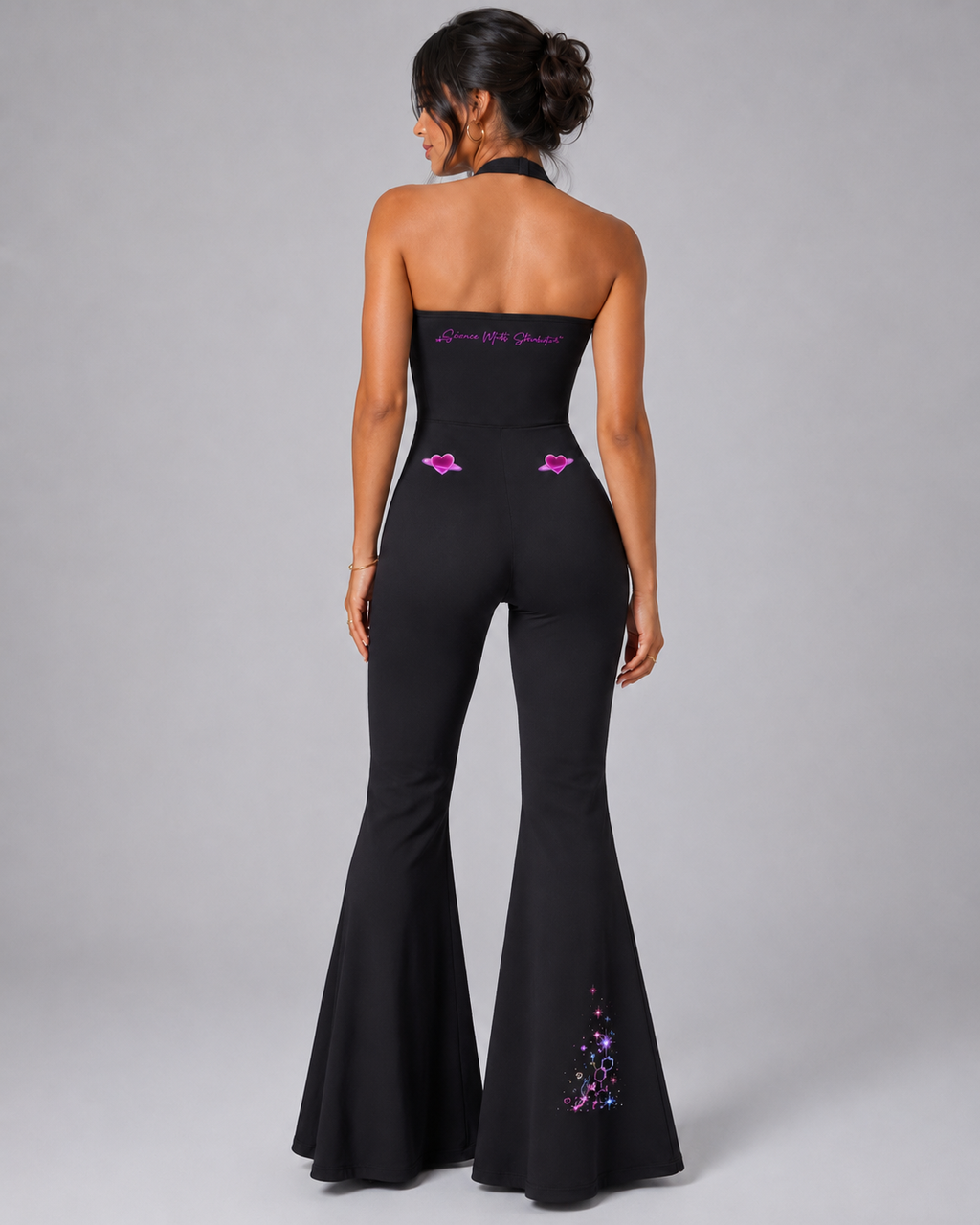 Back studio view of the black Cosmic Heart halter flared jumpsuit with Science Meets Stardust™ script, ringed hearts and right-leg artwork.