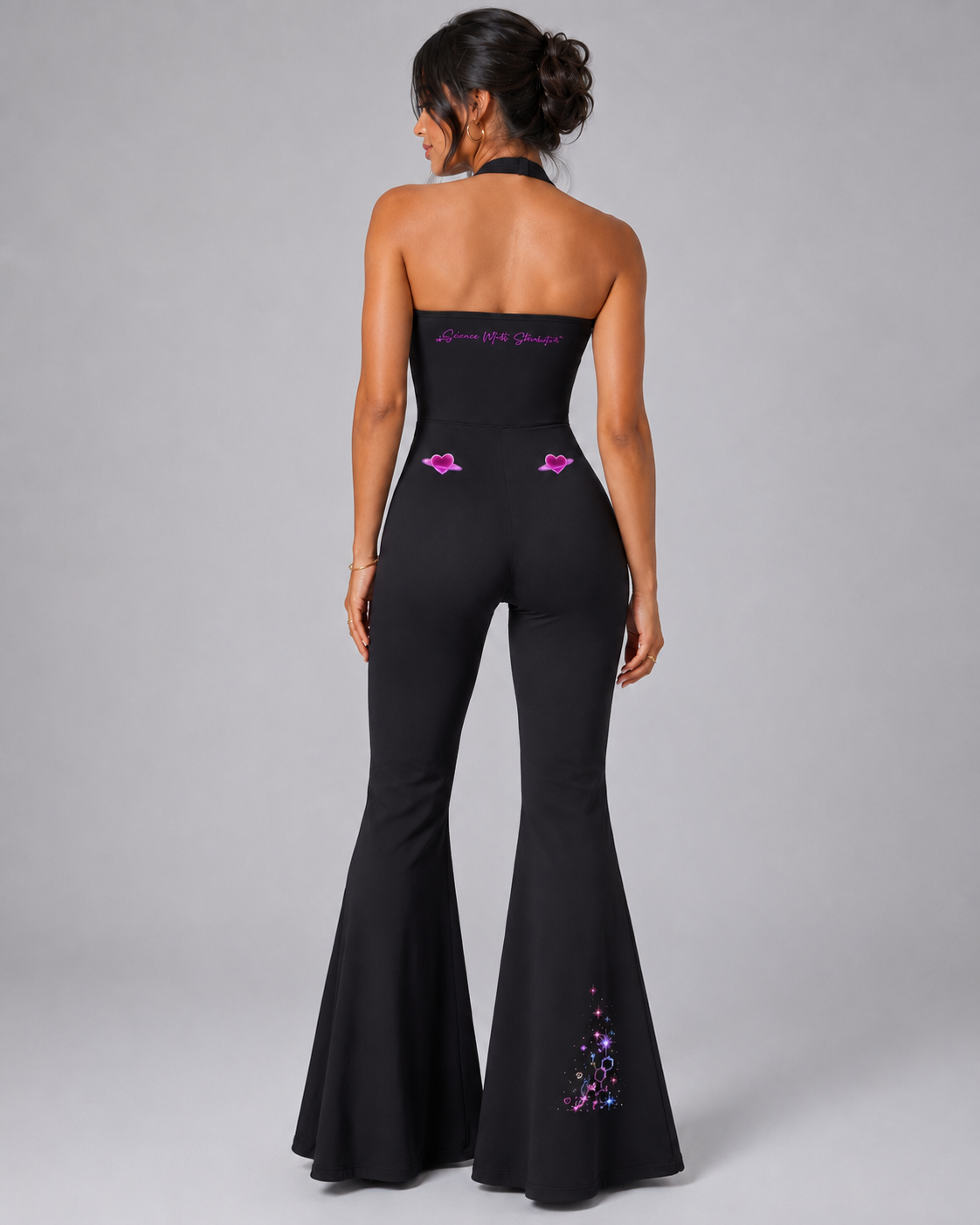 Back studio view of the black Cosmic Heart halter flared jumpsuit with Science Meets Stardust™ script, ringed hearts and right-leg artwork.