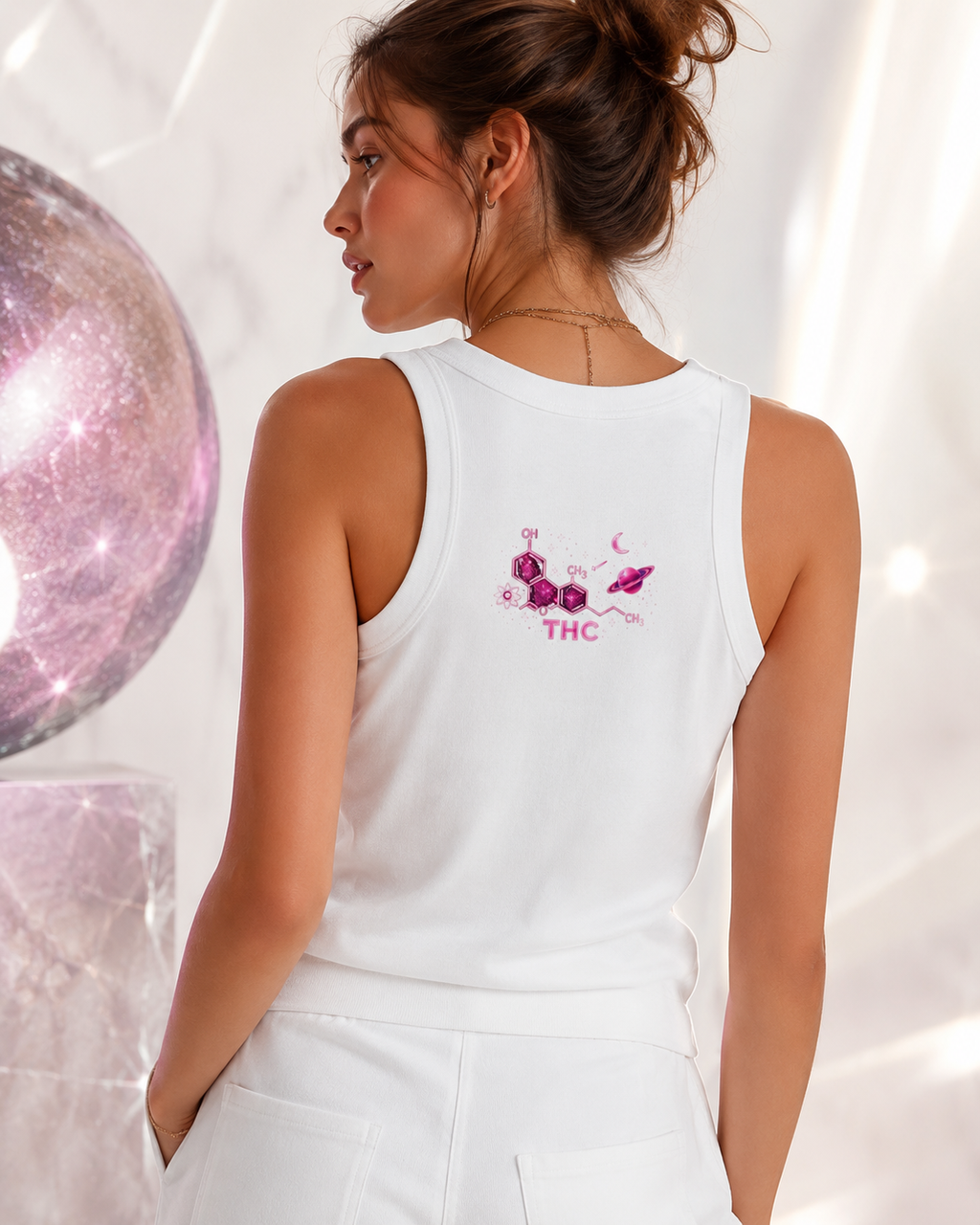 Back lifestyle view of a woman wearing the white crop tank with its pink THC celestial graphic inside a luminous cosmic-inspired interior.