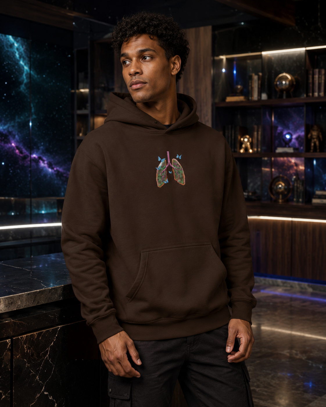 Male model wearing the dark chocolate Butterfly Lungs hoodie in an upscale lounge with dark wood and subtle galaxy accents.