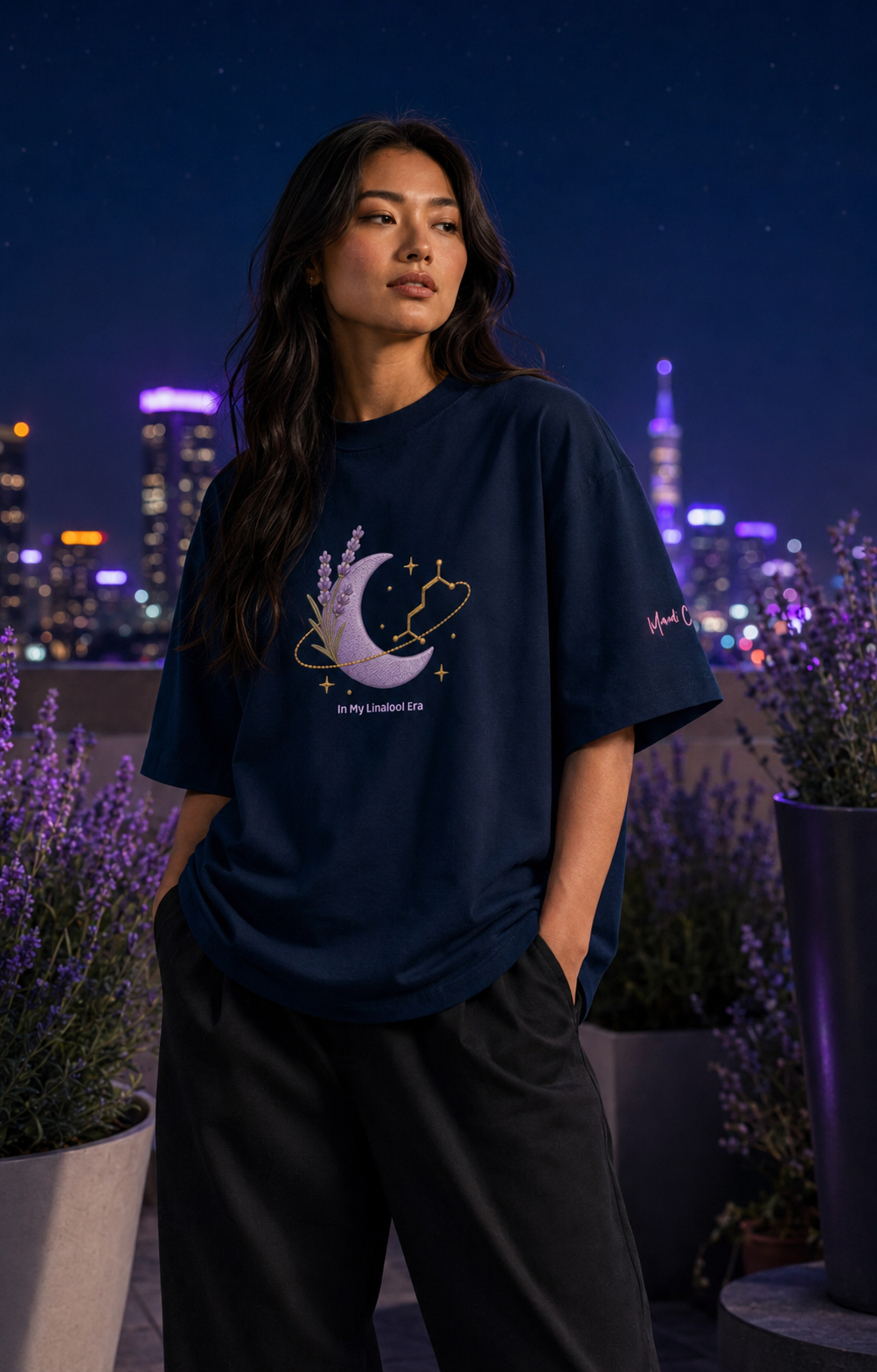 Woman wearing the French-navy In My Linalool Era oversized tee in a rooftop lavender garden at blue hour.