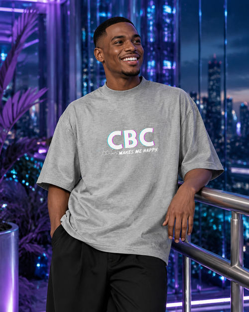 Smiling man wearing the heather grey CBC Makes Me Happy oversized tee in a futuristic violet-lit city setting.