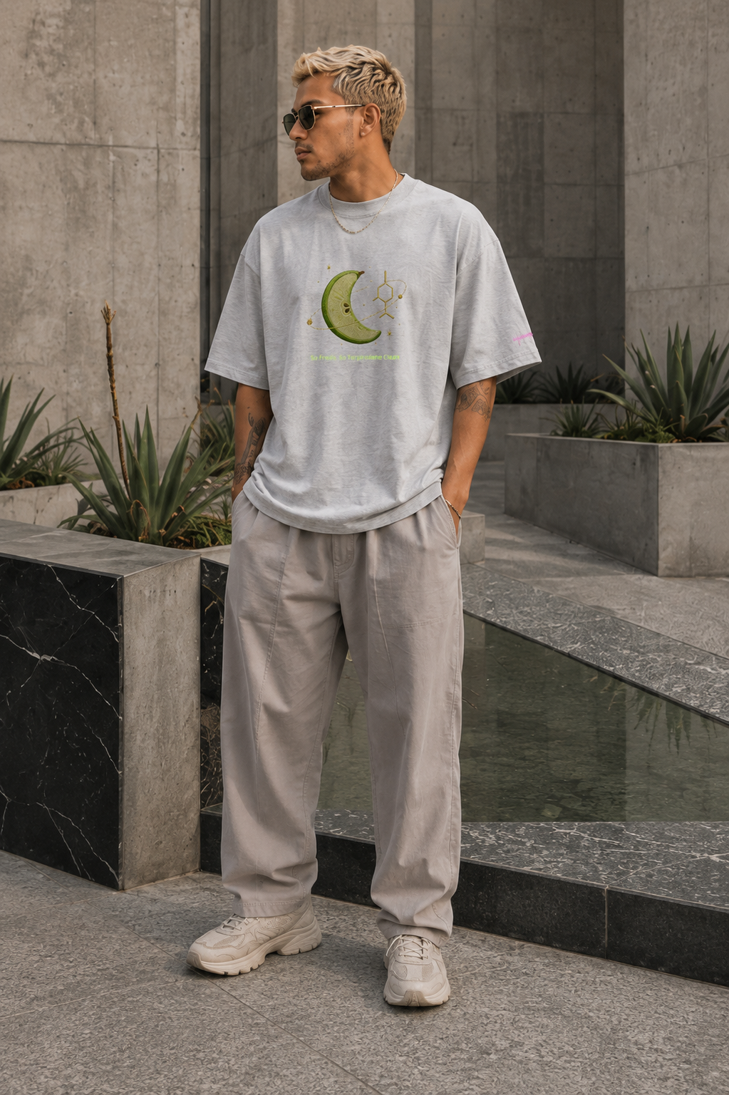 Man wearing the heather-grey So Fresh, So Terpinolene Clean oversized tee in a modern concrete courtyard.