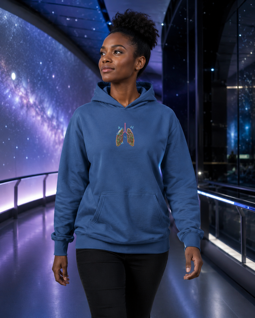 Woman modeling the indigo blue Butterfly Lungs hoodie while walking through a sleek planetarium corridor with a galaxy display.