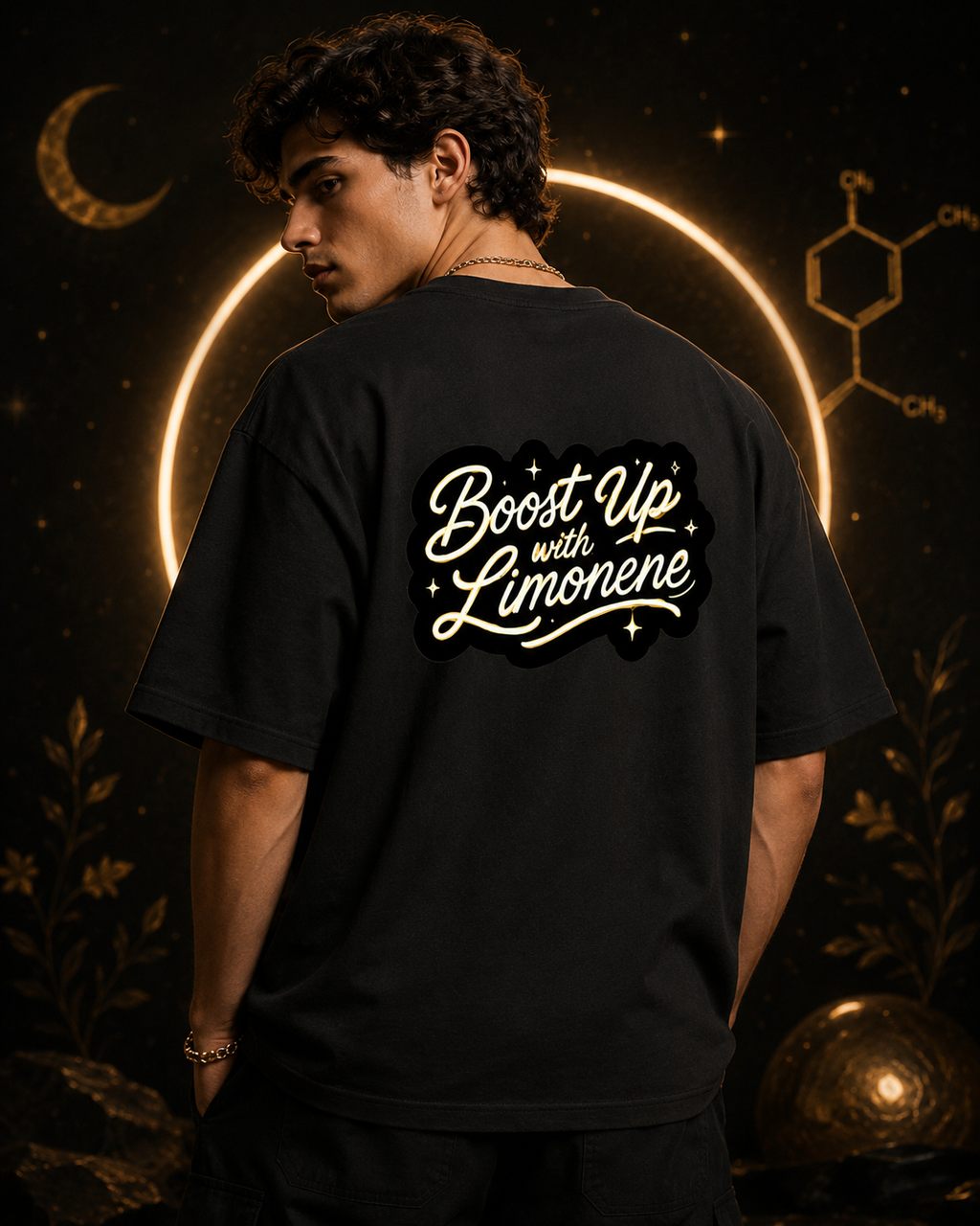 Man modeling the dark-gray Limonene Boost Up oversized tee from the back, displaying the gold script design in a celestial room.