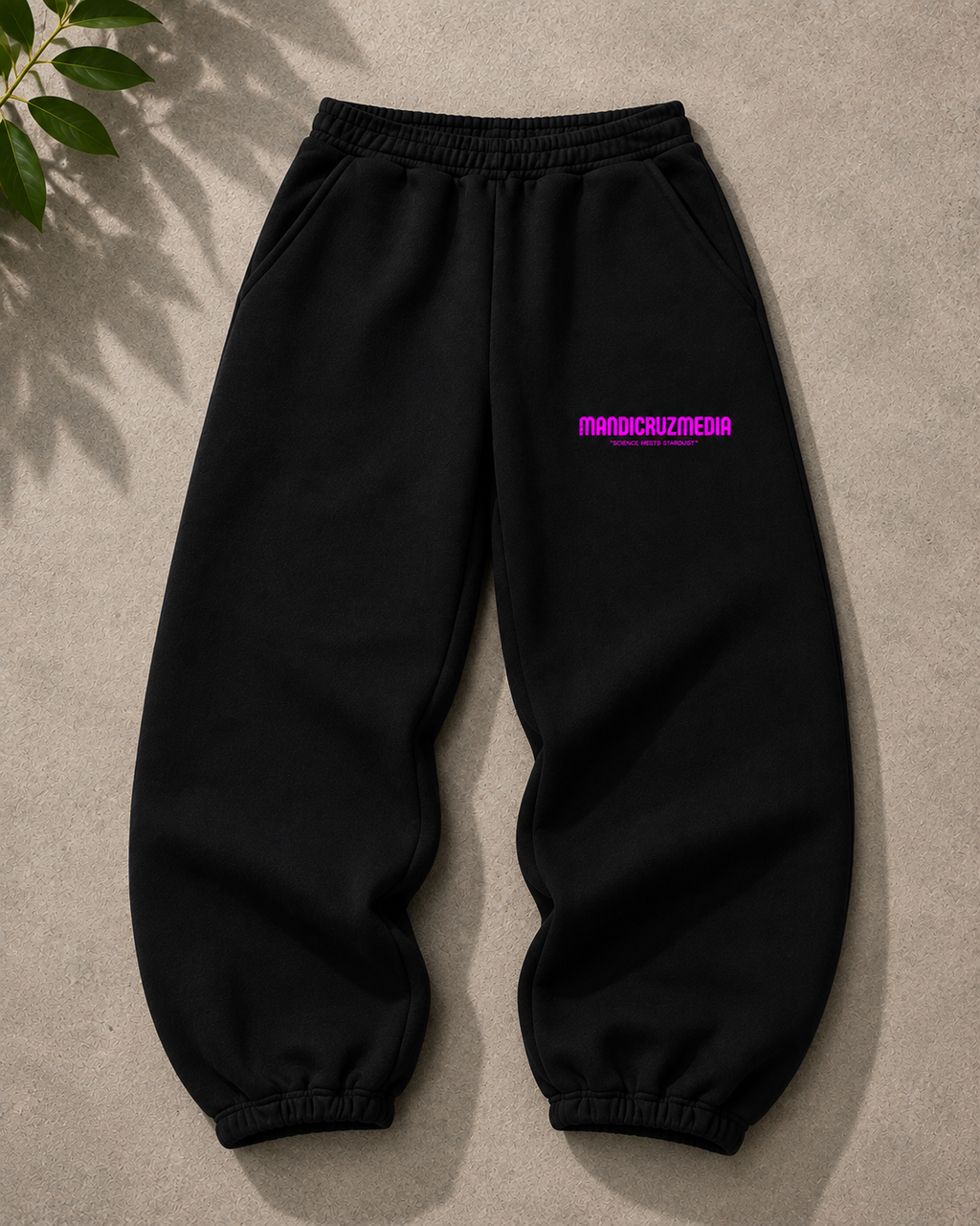 Black oversized fleece sweatpants by Mandi Cruz Media shown from the front with bright pink Mandi Cruz Media branding on the thigh.