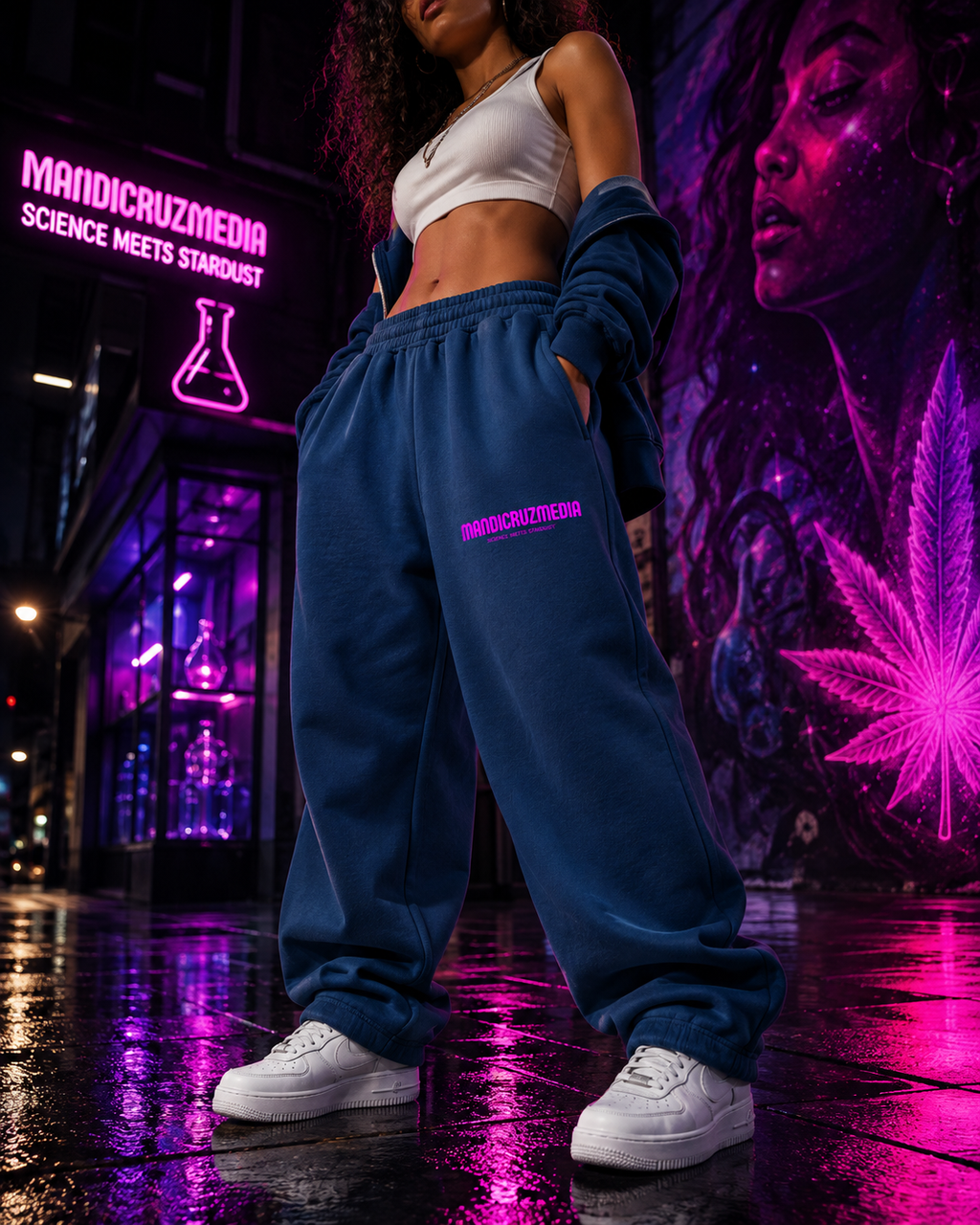 Model wearing blue oversized Mandi Cruz Media fleece sweatpants with pink thigh logo in a neon pink and purple streetwear setting.