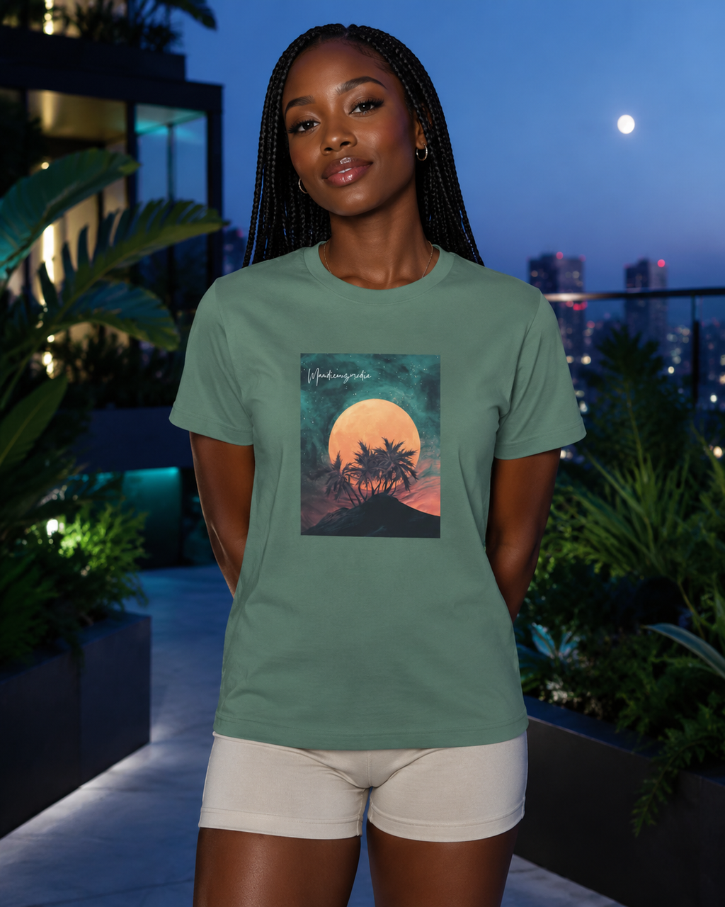 Woman wearing a sage green moon-and-palm graphic T-shirt in a rooftop garden at night.