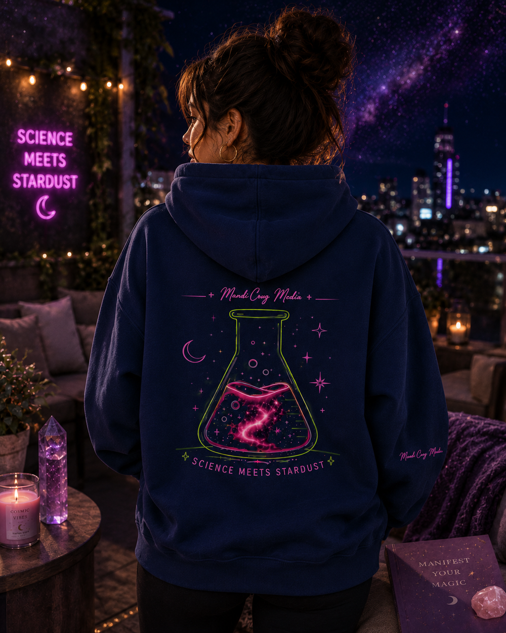 Back view of a woman wearing the navy Mandi Cruz Media hoodie featuring the large neon cosmic flask and Science Meets Stardust graphic against a starry rooftop backdrop.
