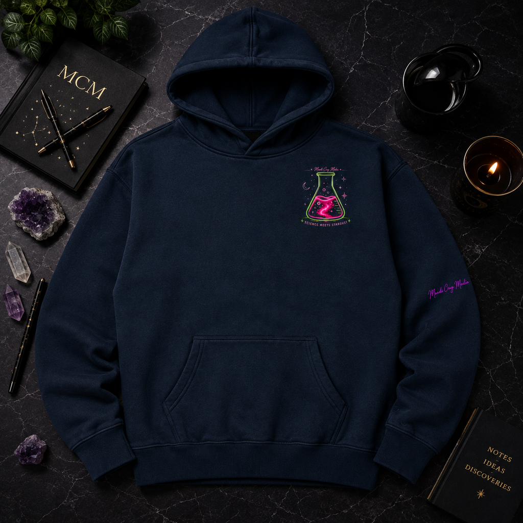 Navy Mandi Cruz Media oversized hoodie displayed in a premium dark flat lay with neon flask chest artwork, crystals, candle, journal and celestial accents.