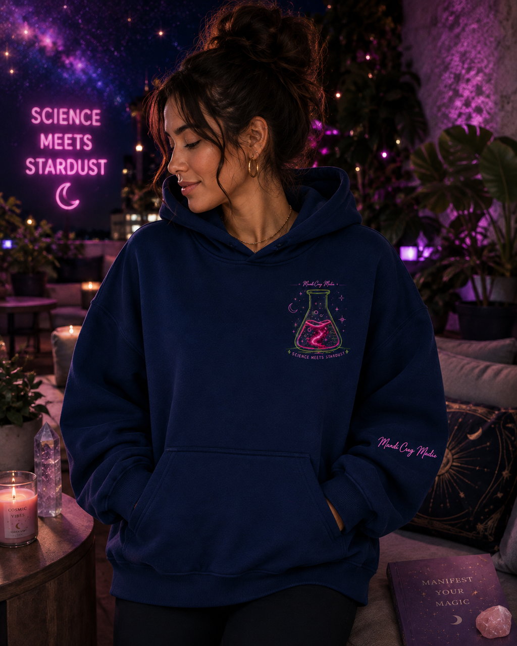 Woman wearing a navy Mandi Cruz Media oversized hoodie with neon Science Meets Stardust flask artwork on the chest in a purple-lit cosmic rooftop setting.