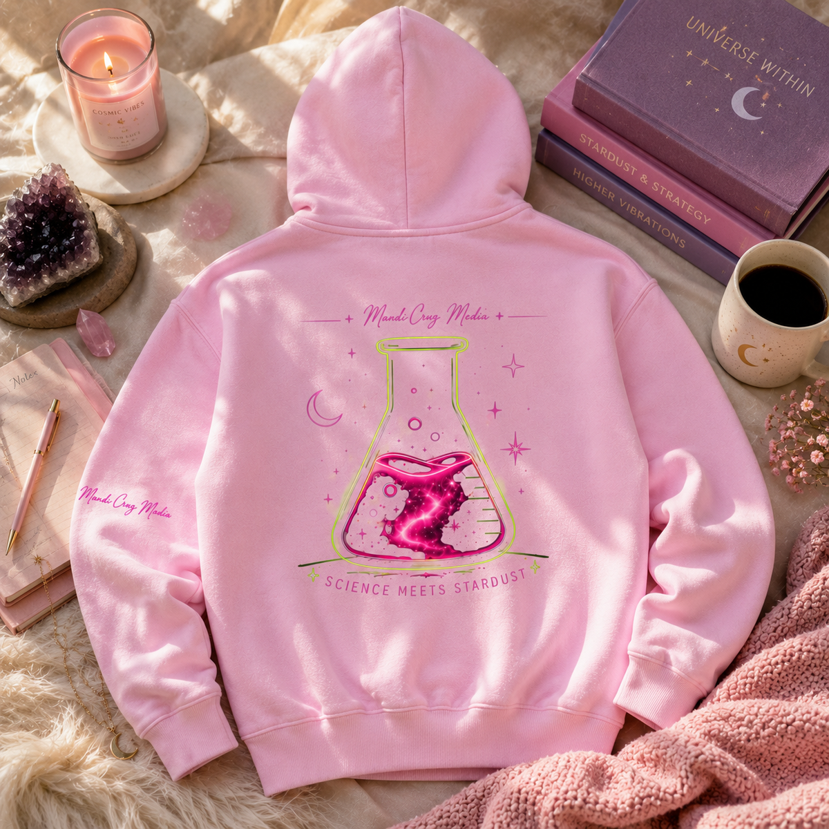 Back of pink Mandi Cruz Media hoodie featuring a large neon flask and galaxy Science Meets Stardust graphic, styled with crystals, candle, journal, and celestial accessories.