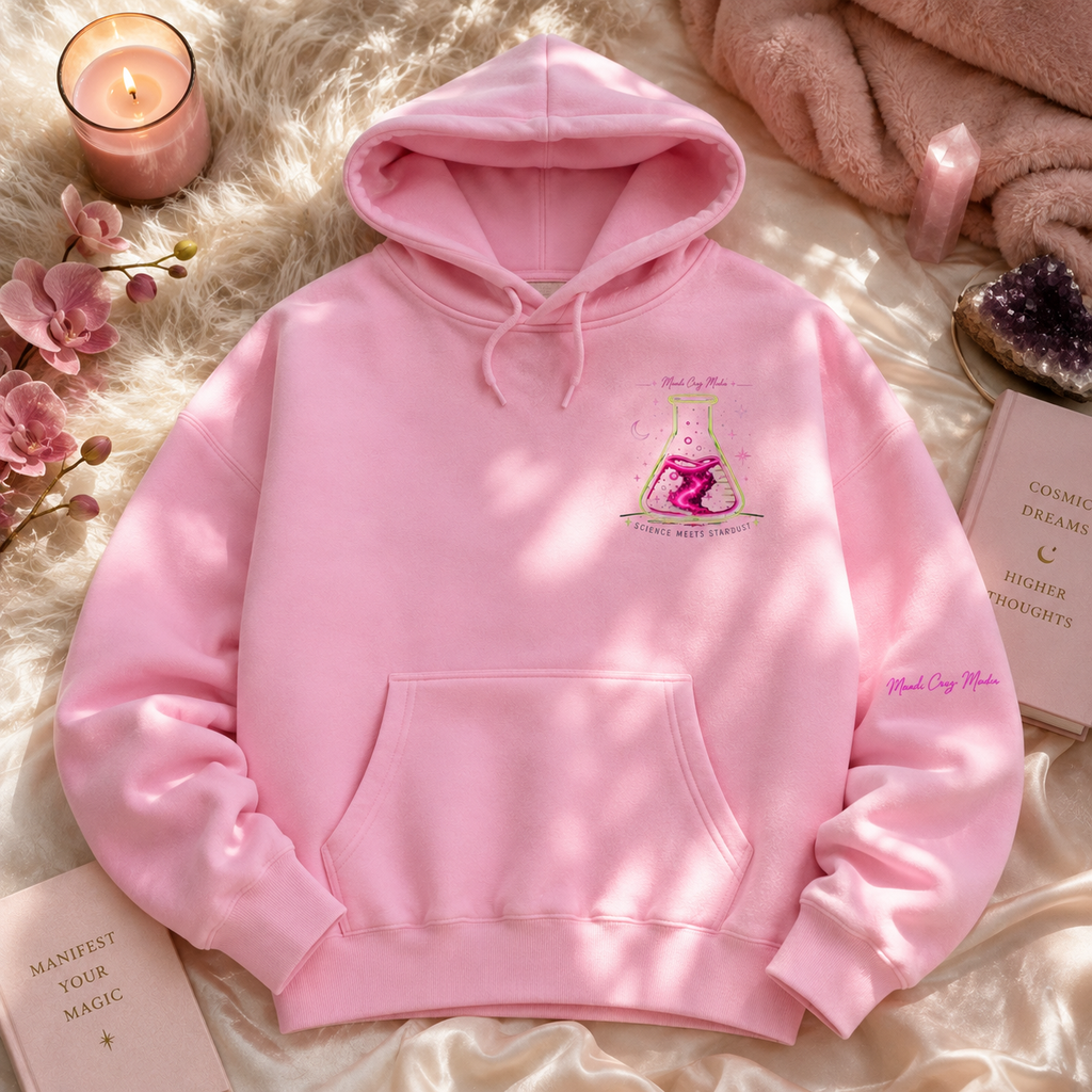 Pink Mandi Cruz Media oversized hoodie shown in a cozy flat lay with the Science Meets Stardust flask chest graphic, pink sleeve branding, crystals, candle, and celestial accessories.