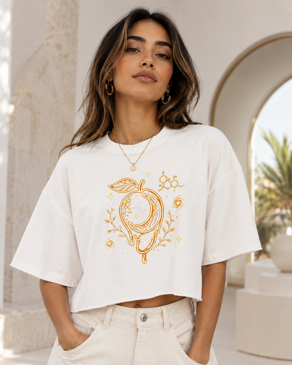 Woman wearing the white raw-hem boxy tee with gold mango moon, botanical and myrcene molecule artwork in a bright neutral setting.