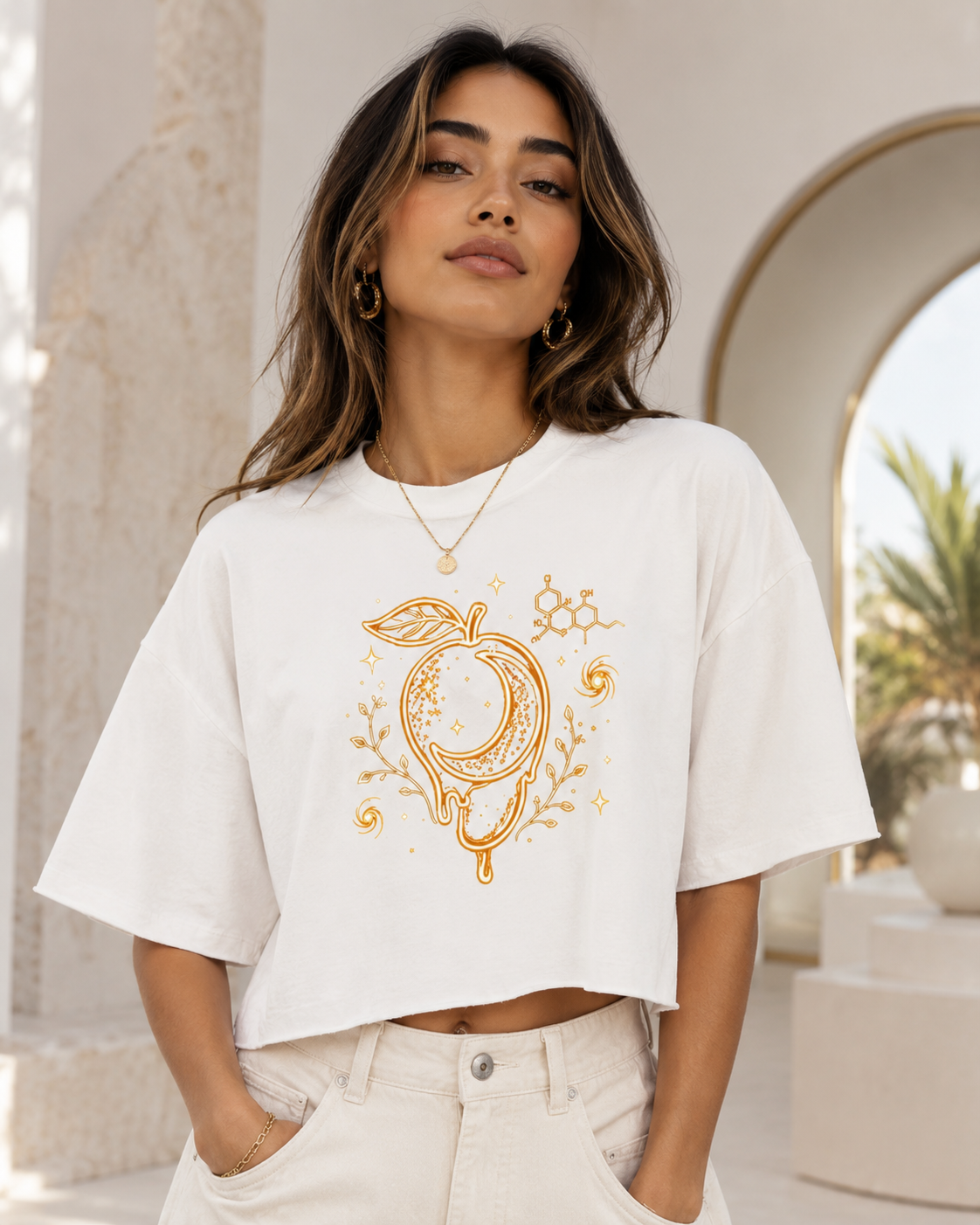 Woman wearing the white raw-hem boxy tee with gold mango moon, botanical and myrcene molecule artwork in a bright neutral setting.