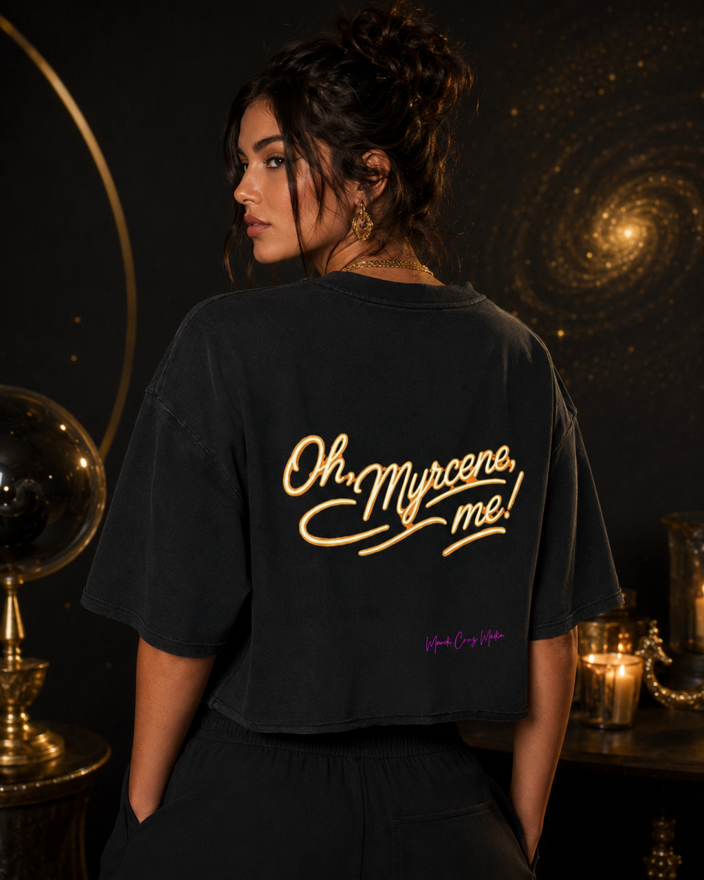 Woman modeling the black Oh, Myrcene, Me! mineral-wash boxy tee from the back in a dark celestial setting with gold accents.