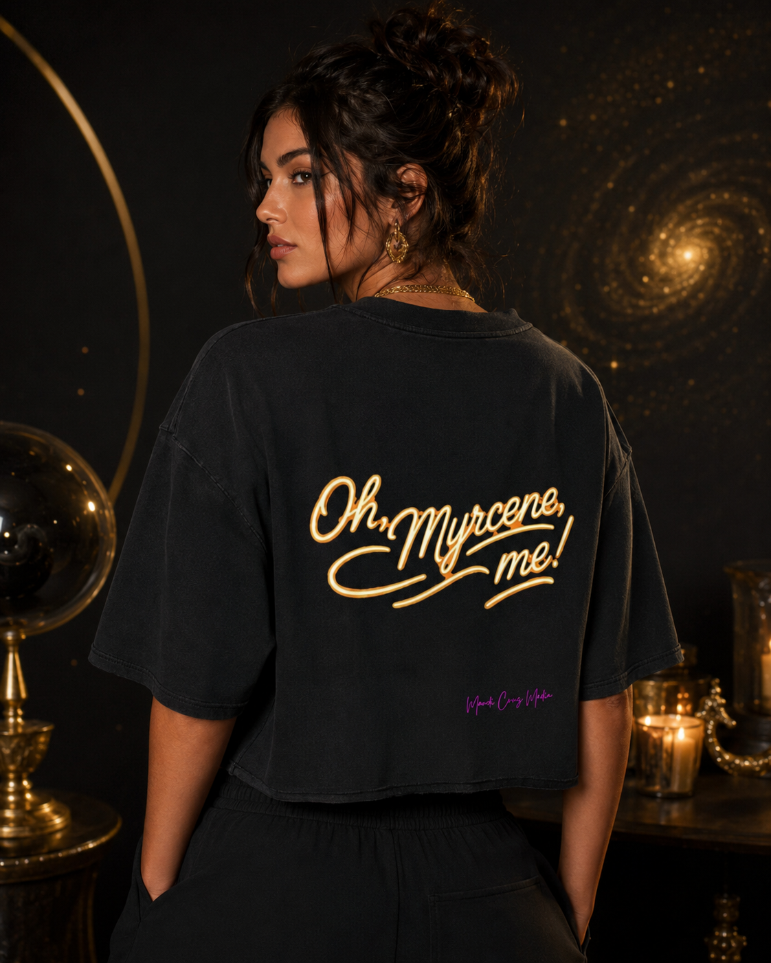 Woman modeling the black Oh, Myrcene, Me! mineral-wash boxy tee from the back in a dark celestial setting with gold accents.