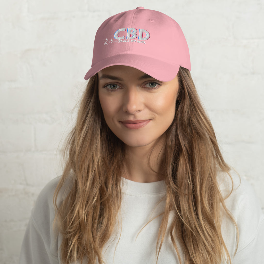 Blonde woman in a white top facing forward while wearing the pink CBD Heals My Hurt embroidered dad hat.