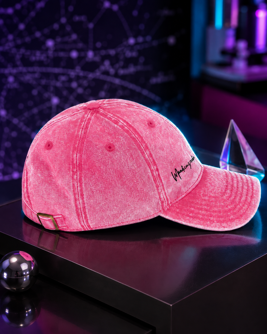 Pink acid-wash cotton twill cap with black Mandi Cruz Media embroidery displayed in a cosmic studio setting.