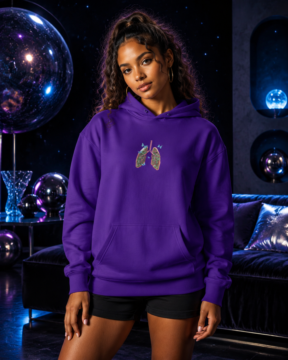 Young woman modeling the purple Butterfly Lungs hoodie with black shorts in a velvet-black cosmic lounge with reflective orbs.
