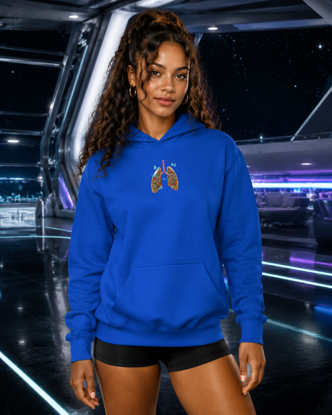 Young woman modeling the royal blue Butterfly Lungs hoodie inside a futuristic silver spaceport lounge with cosmic lighting.