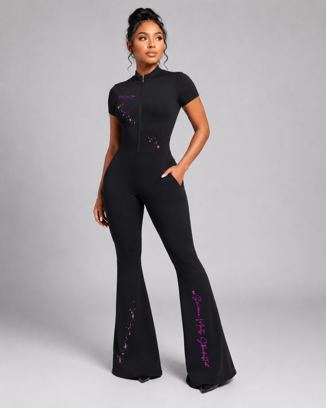 Angled front view of a model wearing the black short-sleeve quarter-zip jumpsuit with a sculpted fit, pockets, flared legs, and pink graphics.