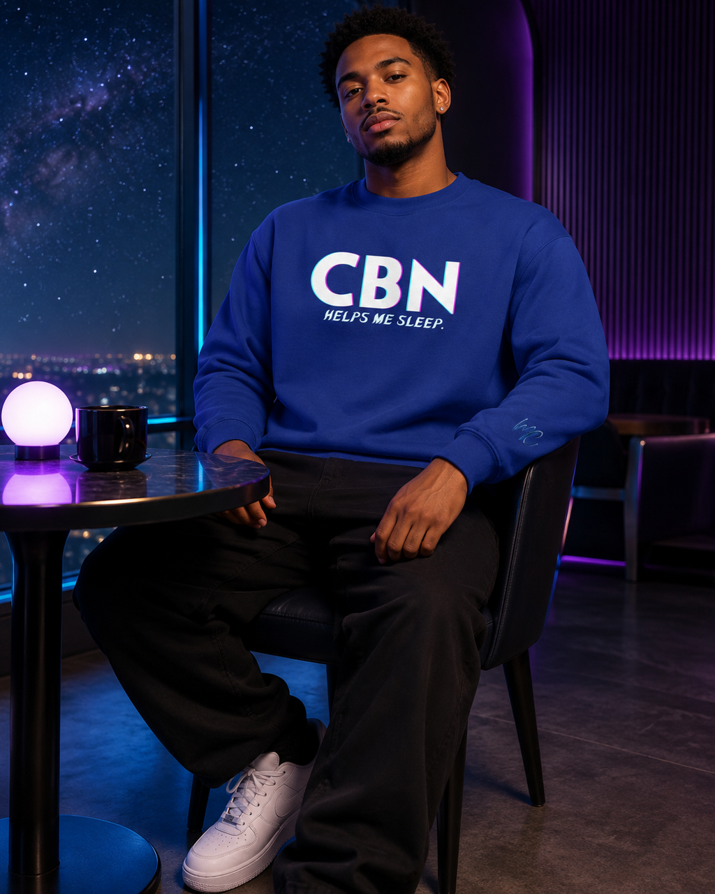 Man wearing a team royal CBN Helps Me Sleep premium sweatshirt with a blue MC sleeve logo in a starlit night lounge.