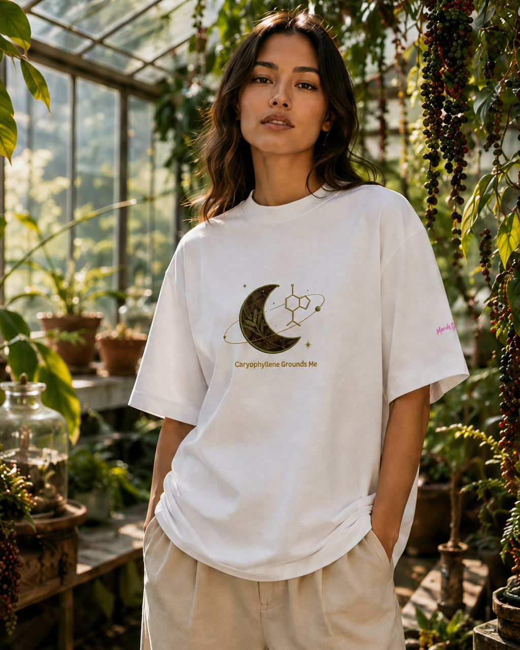 Woman wearing the white Caryophyllene Grounds Me oversized high-neck tee inside a sunlit botanical conservatory.