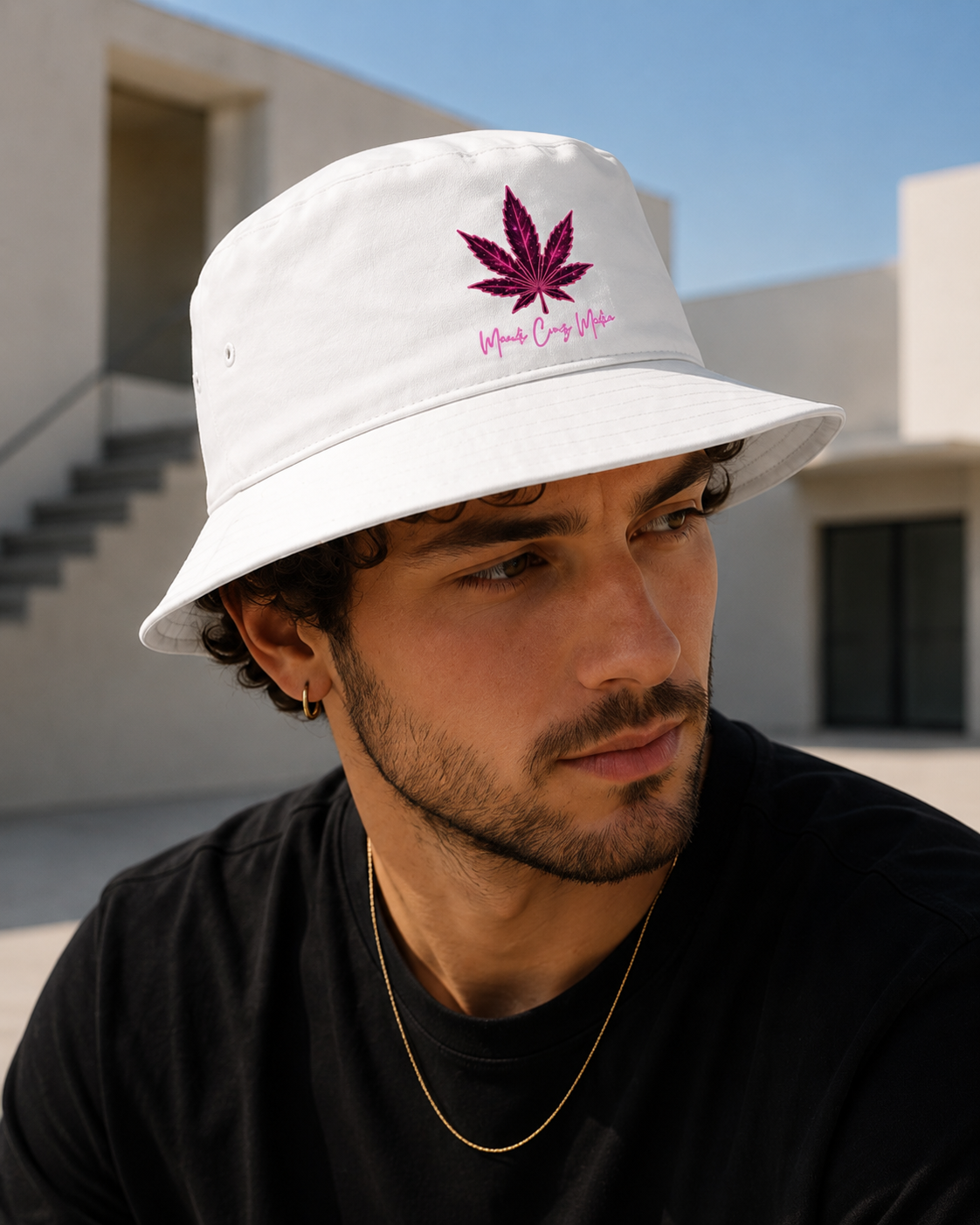 Man wearing the white Mandi Cruz Media Pink Leaf Bucket Hat outdoors beside modern architecture under a blue sky.