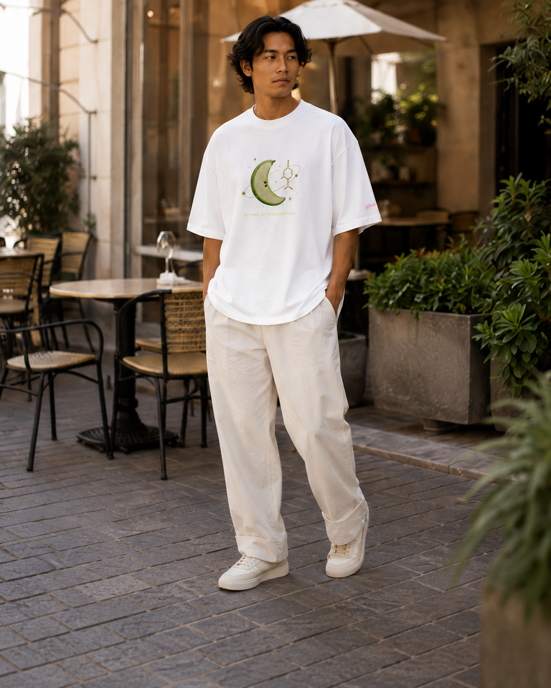 Man modeling the white So Fresh, So Terpinolene Clean oversized tee outside a warm modern café.