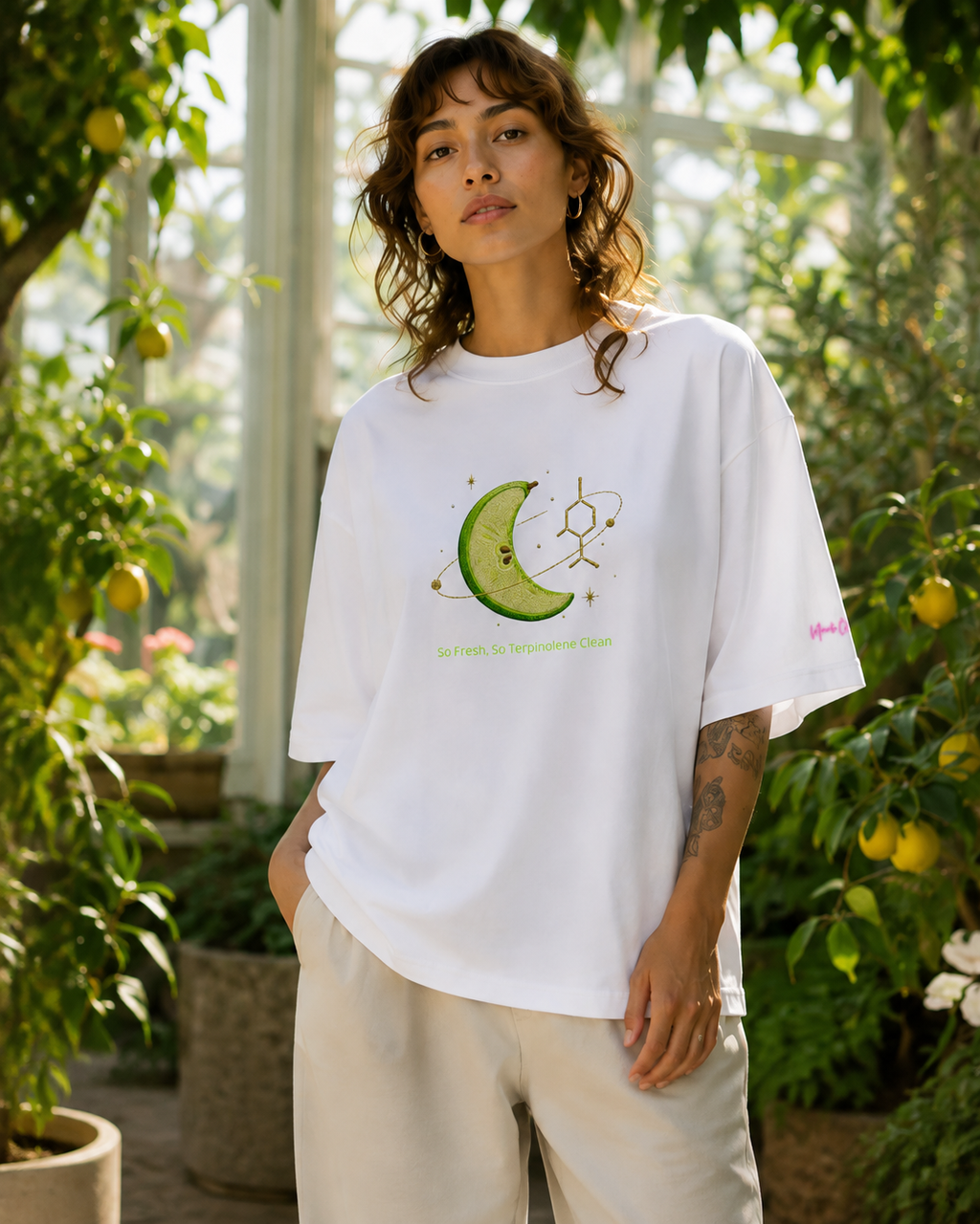 Woman modeling the white So Fresh, So Terpinolene Clean oversized organic tee in a bright citrus greenhouse.