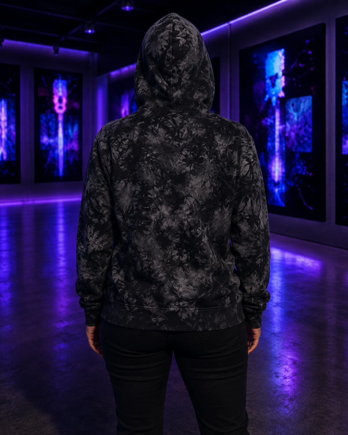 Rear view of a model wearing the Champion tie-dye hoodie with the hood raised in an ultraviolet-lit gallery.