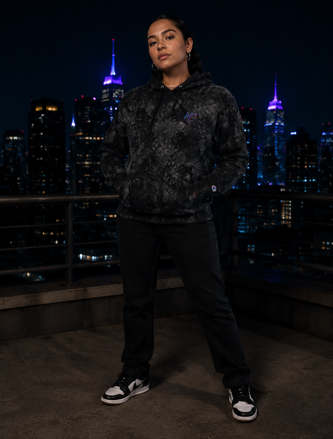 the Mandi Cruz Media Champion tie-dye hoodie on a nighttime city rooftop.