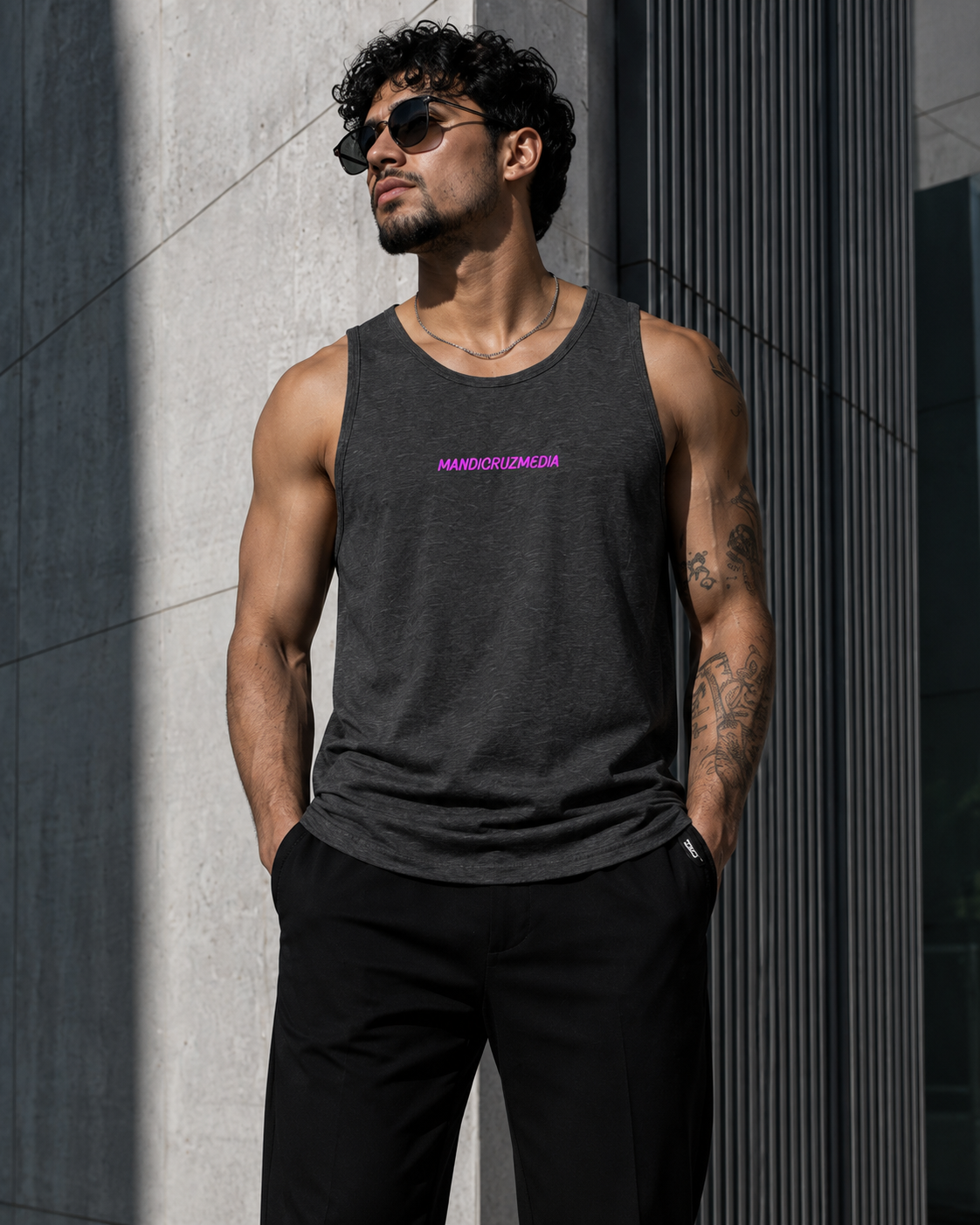 Male model styling the charcoal-heather Mandi Cruz Media premium tank outside contemporary architecture.