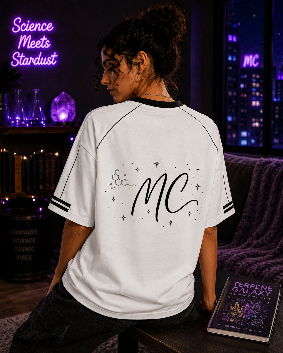 Back lifestyle view of a woman wearing the white Mandi Cruz Media Signature™ Raglan Tee featuring the MC celestial and molecule graphic.