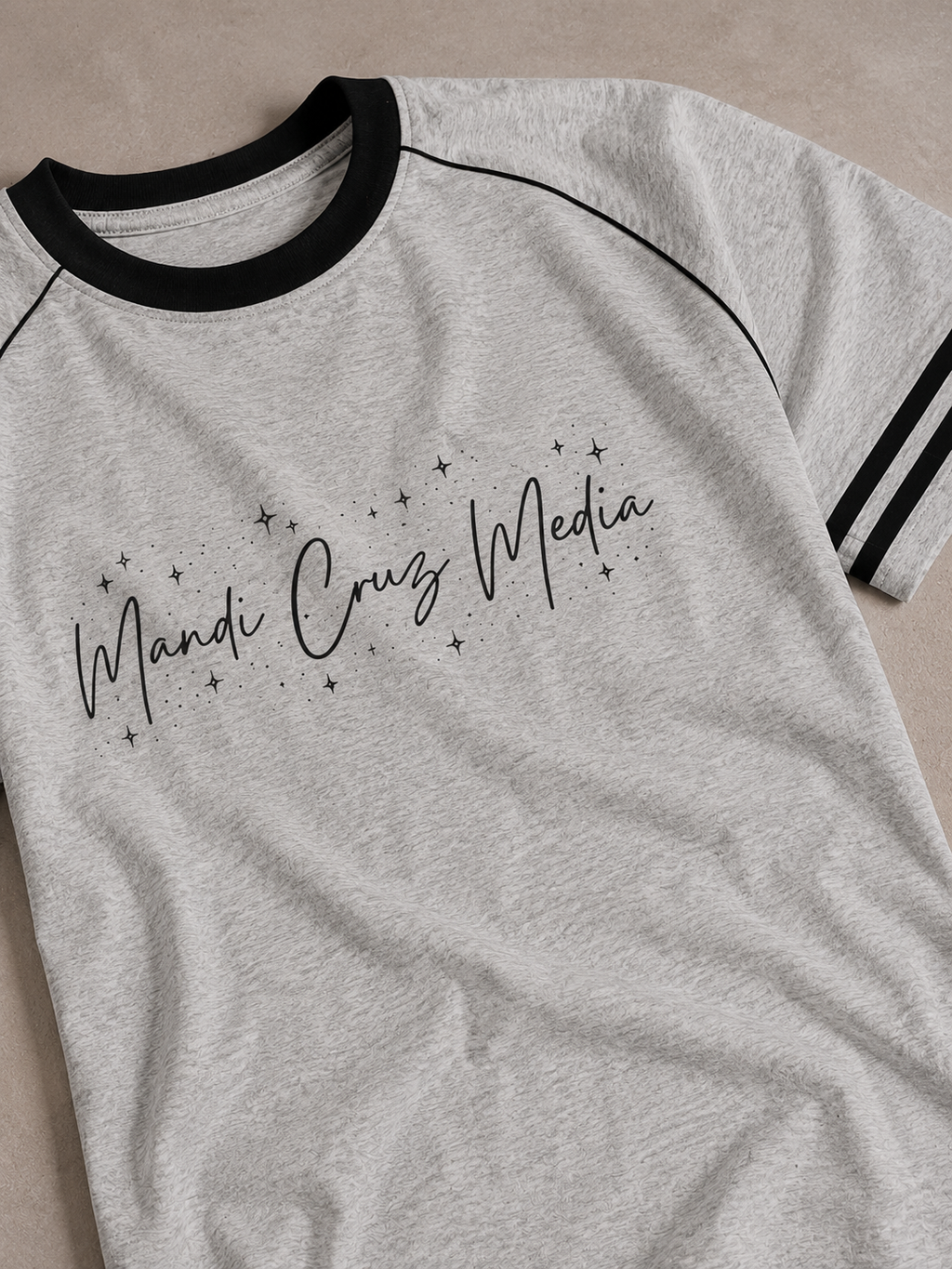 Close-up front view of the light gray Mandi Cruz Media Signature™ Color Block Raglan Tee showing the celestial script graphic, black collar, piping, and striped sleeve detail.
