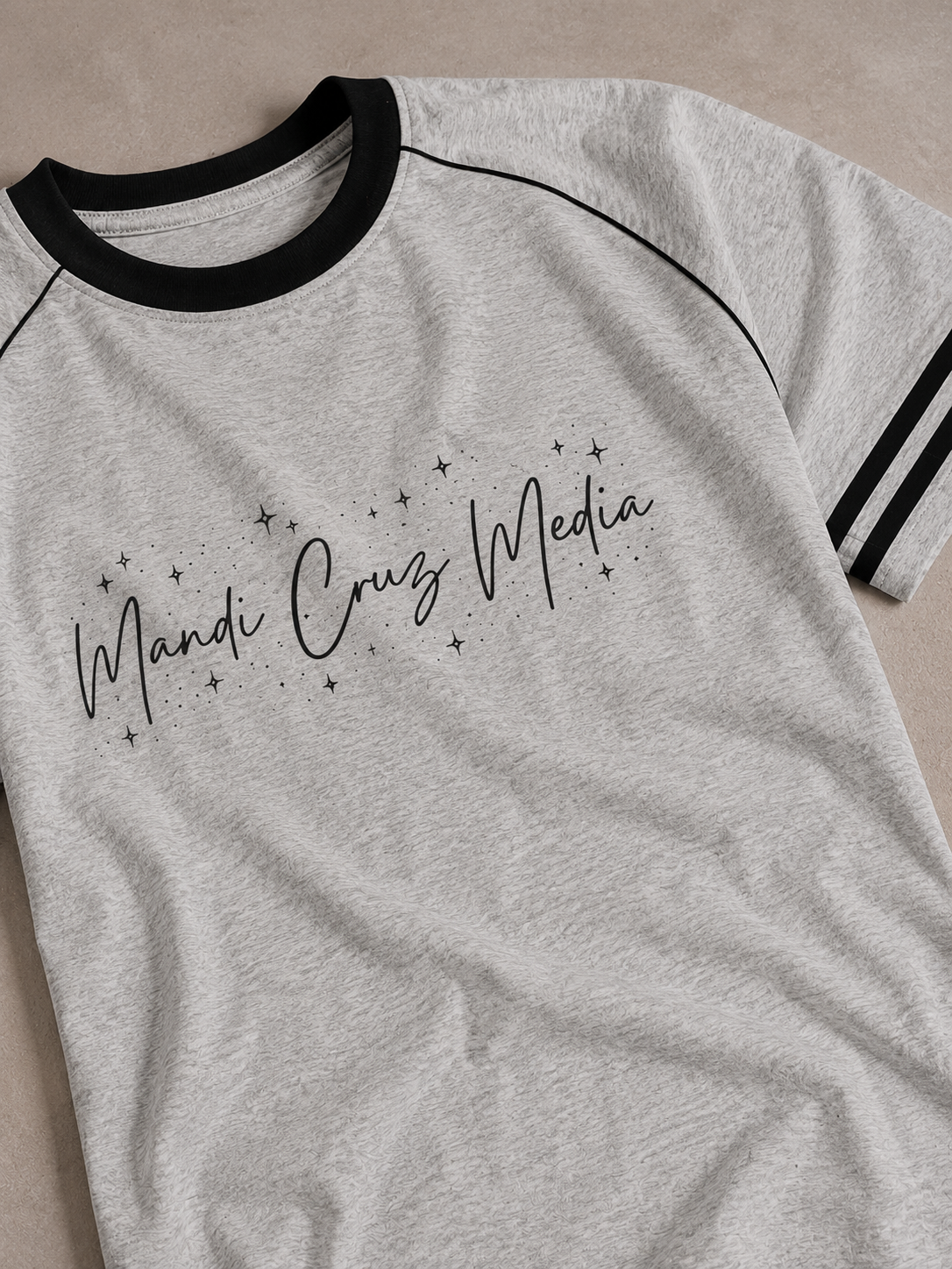 Close-up front view of the light gray Mandi Cruz Media Signature™ Color Block Raglan Tee showing the celestial script graphic, black collar, piping, and striped sleeve detail.