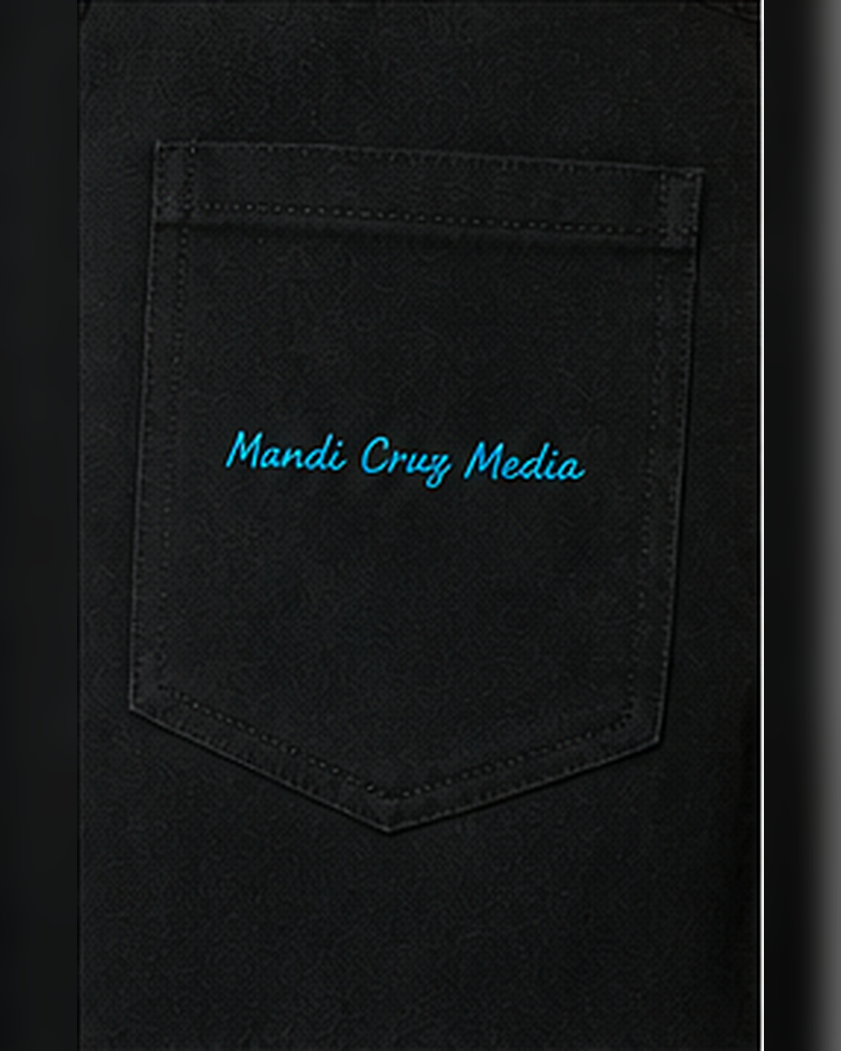 Close-up of the black trouser pocket featuring bright blue embroidered Mandi Cruz Media branding.