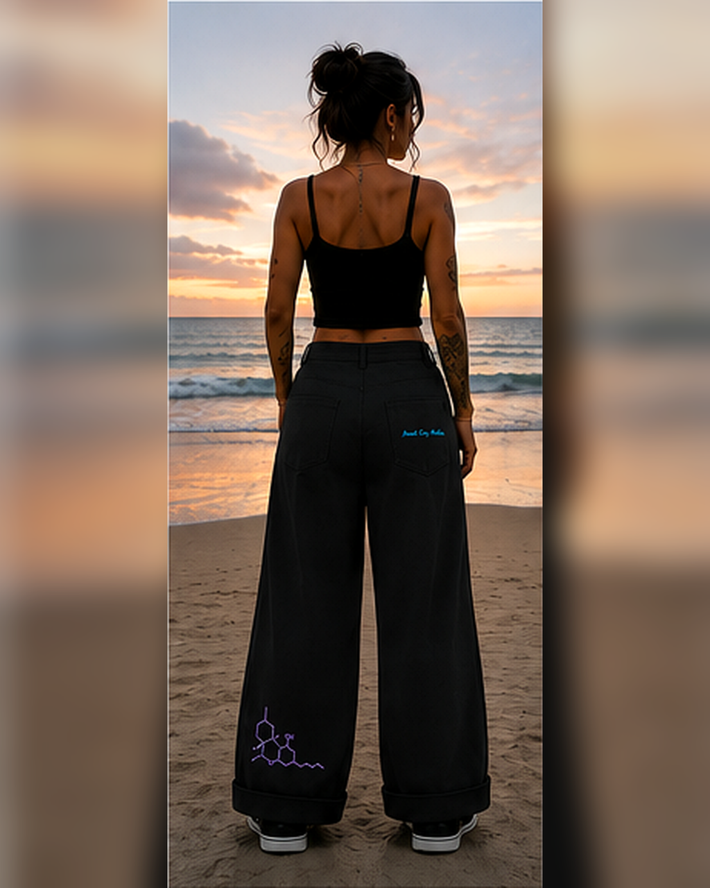 Back lifestyle view of a woman wearing black Mandi Cruz Media wide-leg trousers on a beach at sunset, showing branded back-pocket details.