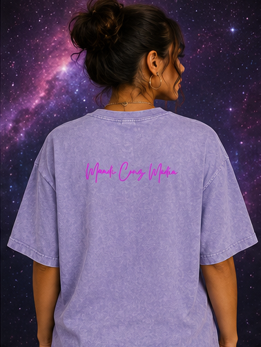 Back lifestyle view of a woman wearing the Light Purple Science Meets Stardust™ oversized acid wash tee featuring the pink Mandi Cruz Media script logo against a galaxy-inspired background.